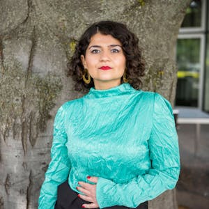 Die Regisseurin Pınar Karabulut posiert vor einem Baumstamm. Sie trägt eine türkis-schimmernde Bluse.&nbsp;