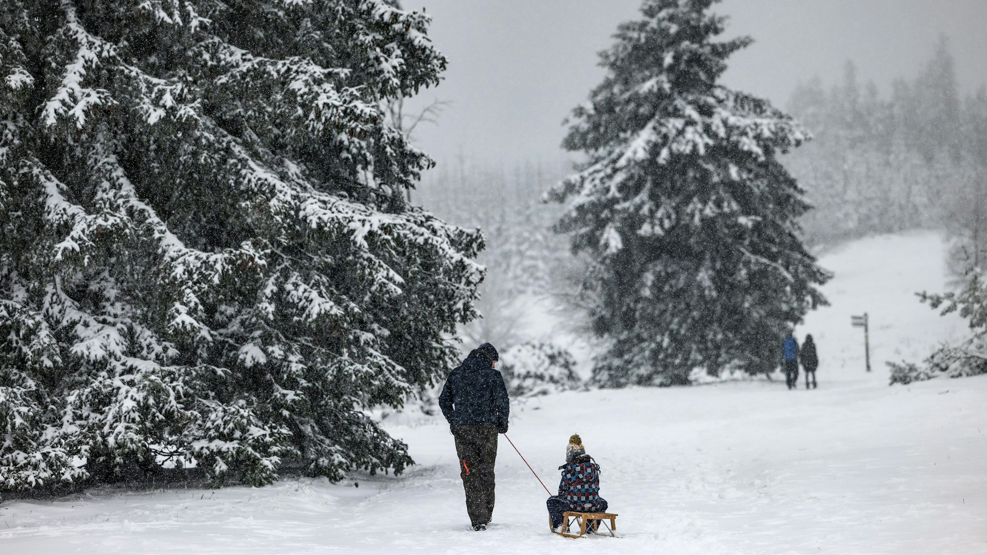 Ein Mann geht mit seinem Kind und einem Schlitten durch den Schnee über den Kahlen Asten.