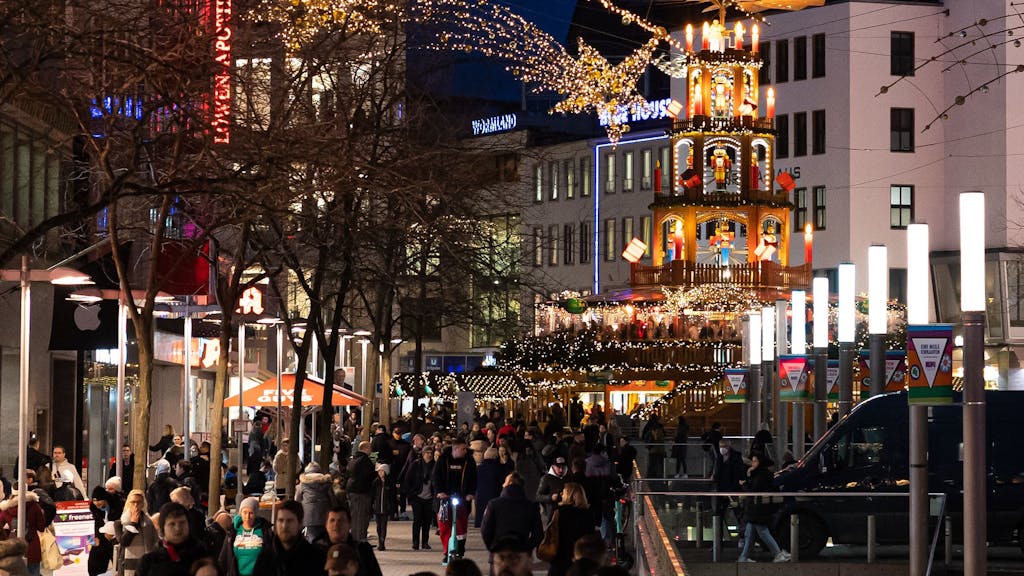 Passanten laufen 2022 durch die Fußgängerzone in der Innenstadt von Hannover. Im Hintergrund steht eine Weihnachtspyramide am Kröpcke, einem zentralen Platz in der Innenstadt.