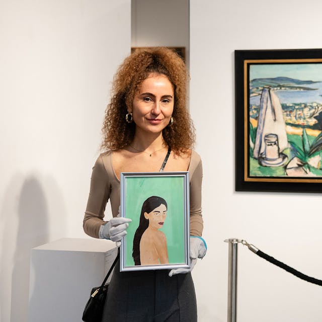 Die Künstlerin hält ihr Bild mit weißen Handschuhen in die Kamera. Neben ihr das Gemälde „Monte Carlo“ von Max Beckmann.