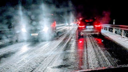 Auf einer Landstraße im Kreis Euskirchen fahren mehrere Autos bei Nacht über eine vereiste Straße. Am Straßenrand liegt Schnee. (Archivbild)