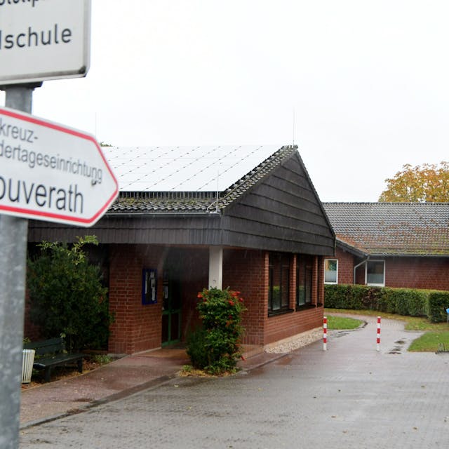 Auf einem Wegweiser steht "Rotkreuz-Kindertageseinrichtung Houverath", dahinter ist der Kindergarten zu sehen.