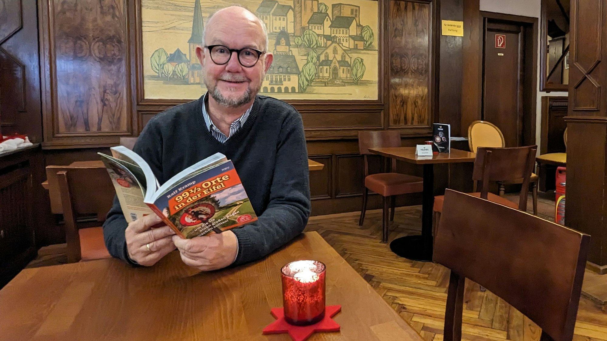 Ralf Kramp sitzt mit seinem neuen Buch an einem Tisch im Café Kramer in Euskirchen.