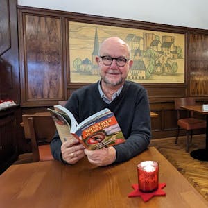 Autor und Verleger Ralf Kramp sitzt mit einem aufgeschlagenen Buch im Café Kramer in Euskirchen.