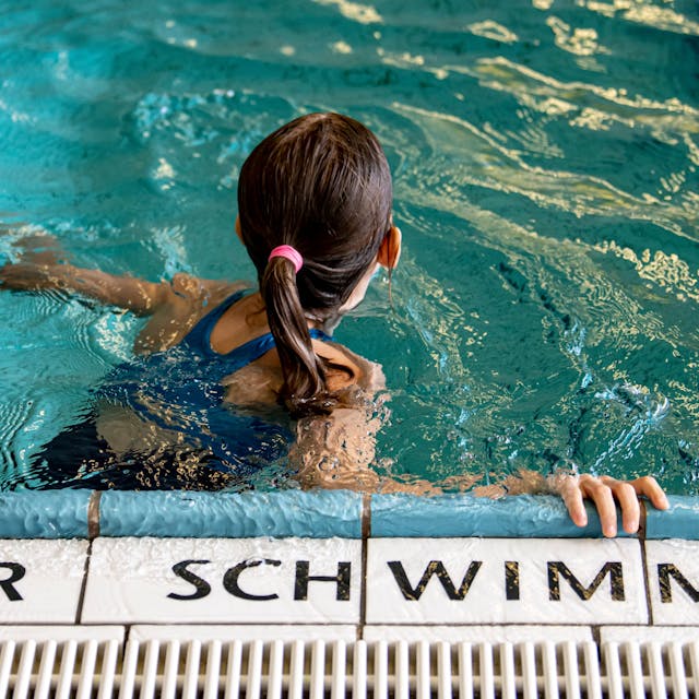 Ein Kind schwimmt in einem Schwimmbad. Auf den Fliesen steht die Aufschrift „Nur für Schwimmer“.&nbsp;