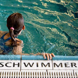 Ein Kind schwimmt in einem Schwimmbad. Auf den Fliesen steht die Aufschrift „Nur für Schwimmer“.&nbsp;