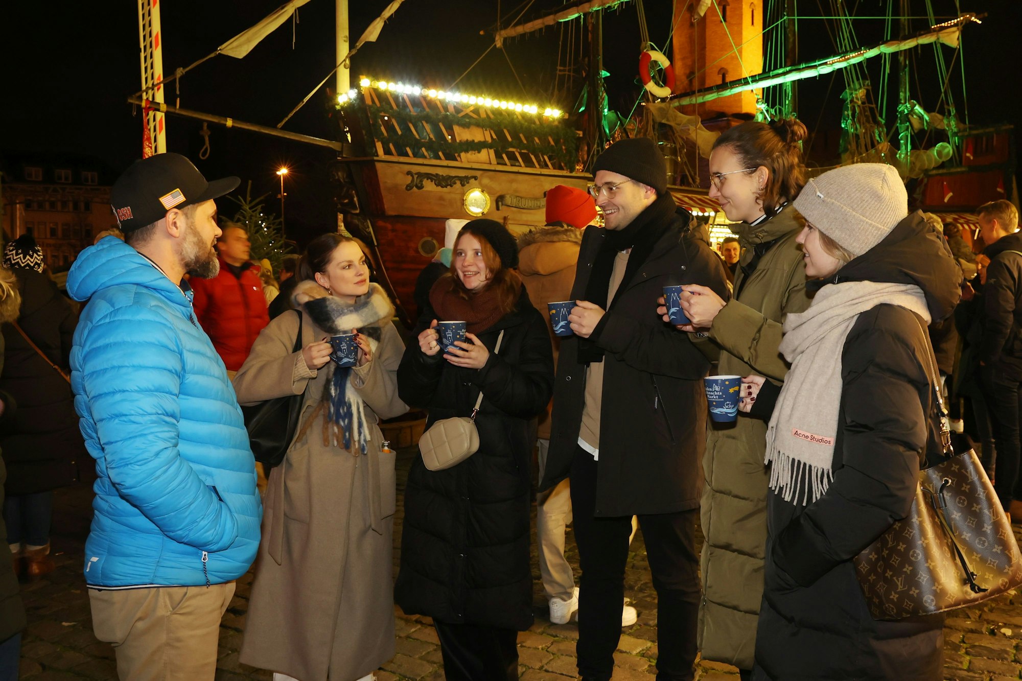 Roman Bendt steht im Halbkreis mit fünf jungen Menschen auf dem Weihnachtsmarkt, sie halten Glühweintassen in der Hand.
