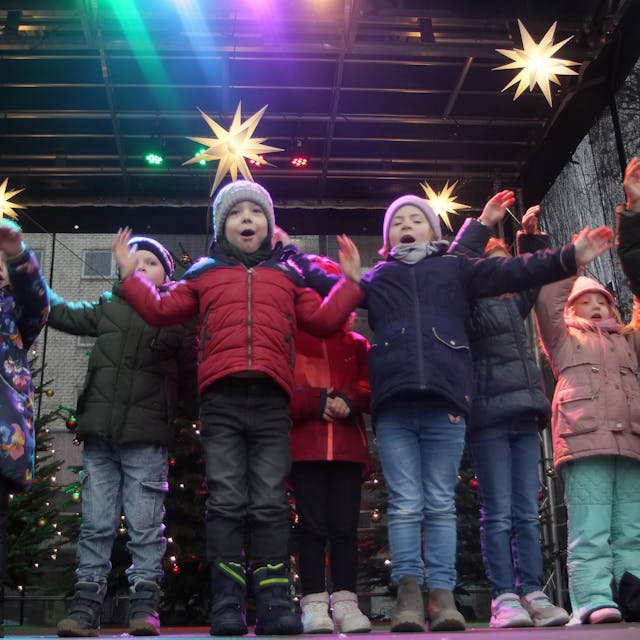 Kinder stehen auf einer weihnachtlich geschmückten Bühne.