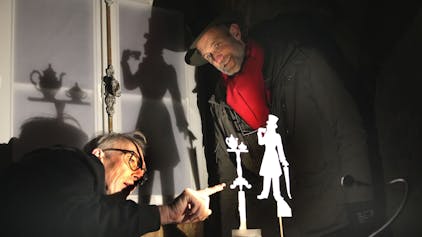 Zwei Männer begutachten eine kleine, aus Papier ausgeschnittene Figur