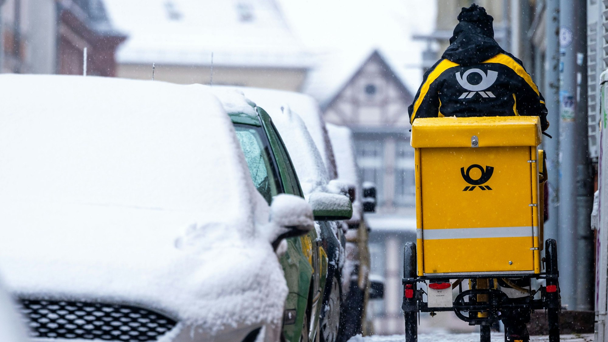 Eine Briefträgerin ist mit ihrem Fahrrad bei starkem Schneefall unterwegs.