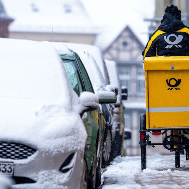 Eine Briefträgerin ist mit ihrem Fahrrad bei starkem Schneefall unterwegs.