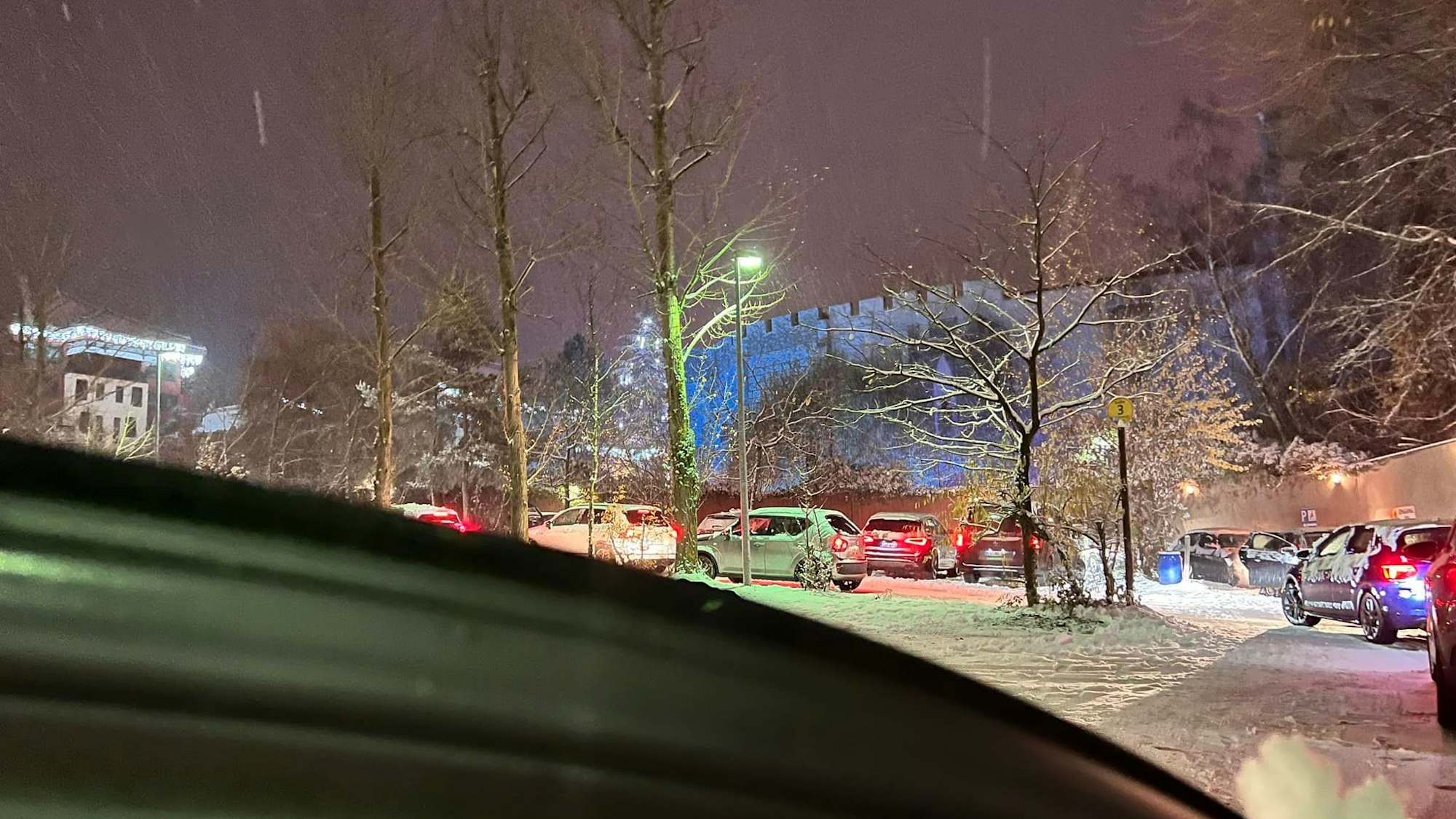 Auf dem Foto ist der tief verschneite Parkplatz des Freizeitparks Phantasialands zu sehen. Autos stehen in der Schlange mit laufenden Motoren.