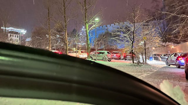 Auf dem Foto ist der tief verschneite Parkplatz des Freizeitparks Phantasialands zu sehen. Autos stehen in der Schlange mit laufenden Motoren.