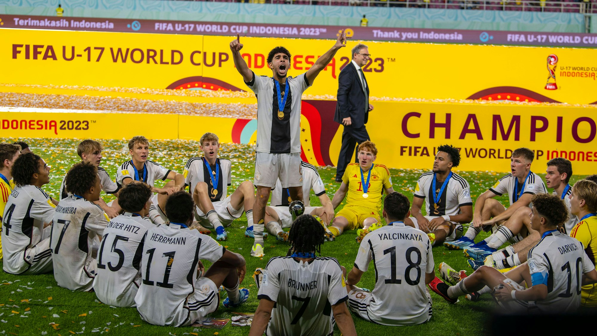 Fußballer mit Medaillen um den Hals sitzen um einen Mannschaftskameraden herum, der stehend jubelt.