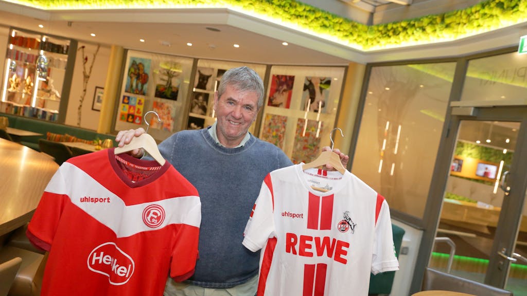 Friedhelm Funkel hält zwei Trikots von Fortuna Düsseldorf und dem 1. FC Köln in die Kamera.&nbsp;