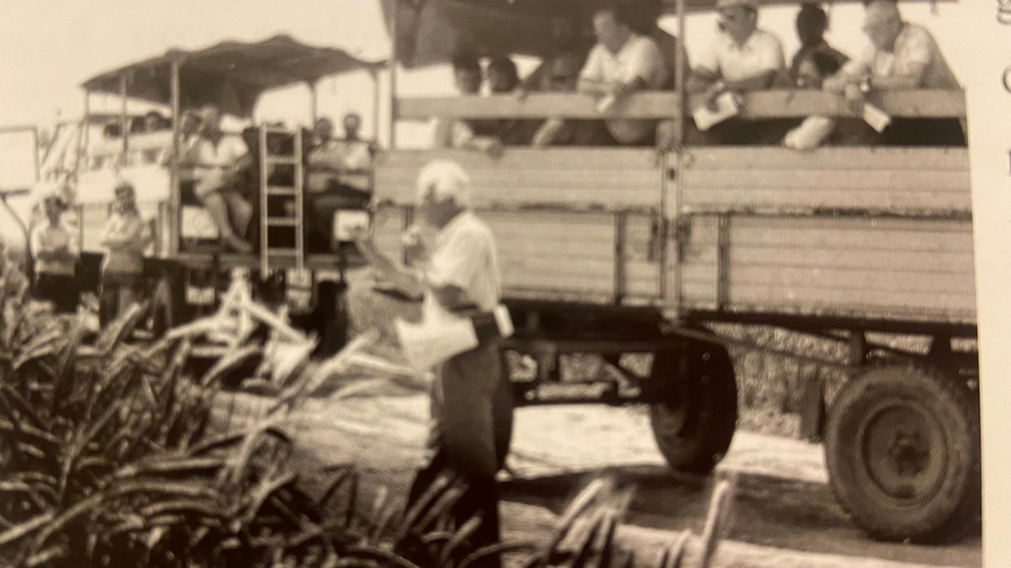 Auf einem Schwarz-Weiß-Bild stehen Männer auf offenen Lkws an einem Feldrand.