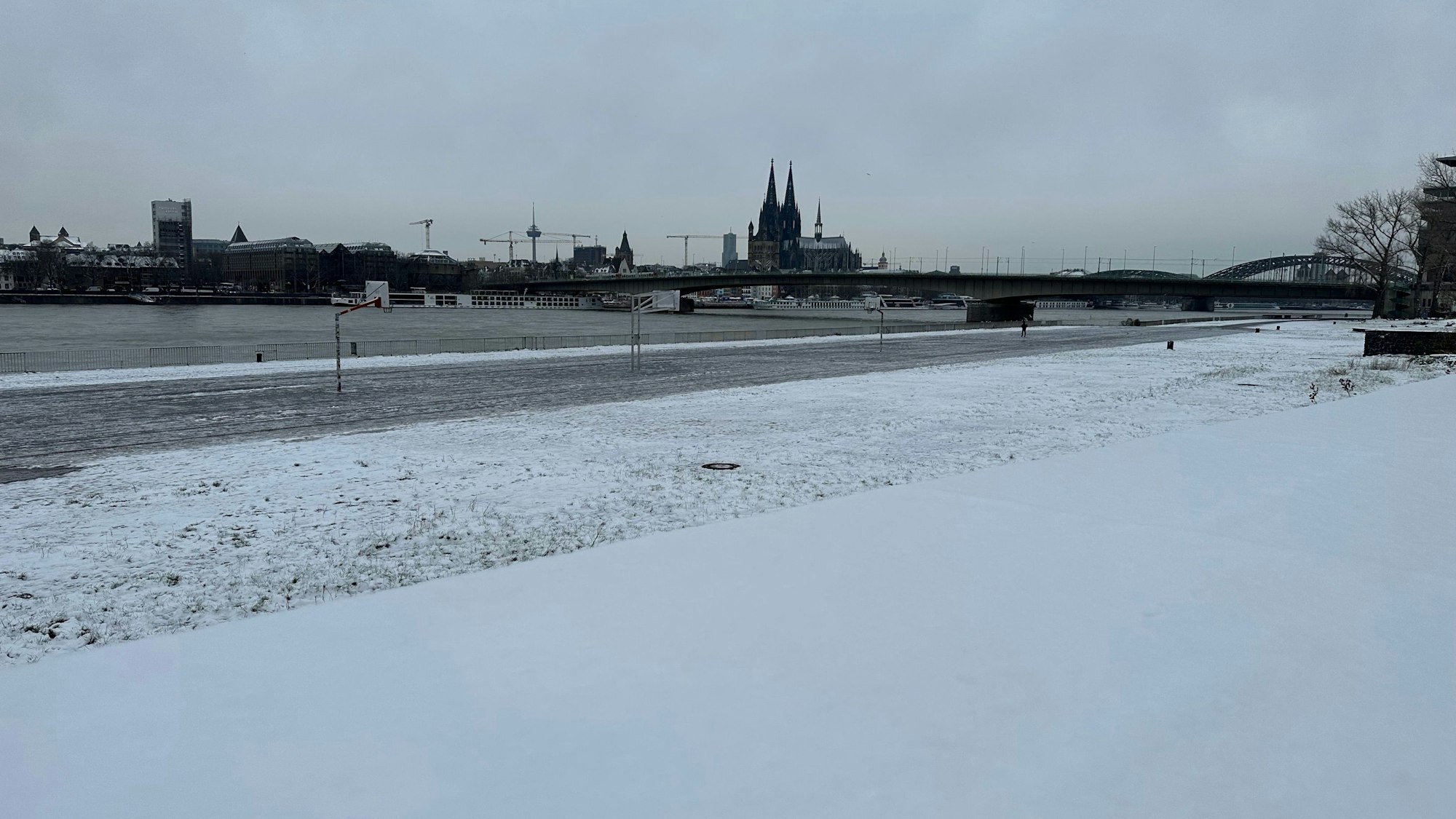 Am Montag, 4. Dezember, liegt noch eine leichte Schneedecke über einigen Teilen Kölns. Am Rhein sind Grünflächen mit Schnee bedeckt.