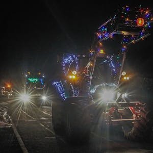 Ein beleuchteter Traktor fährt durch ein Dorf.