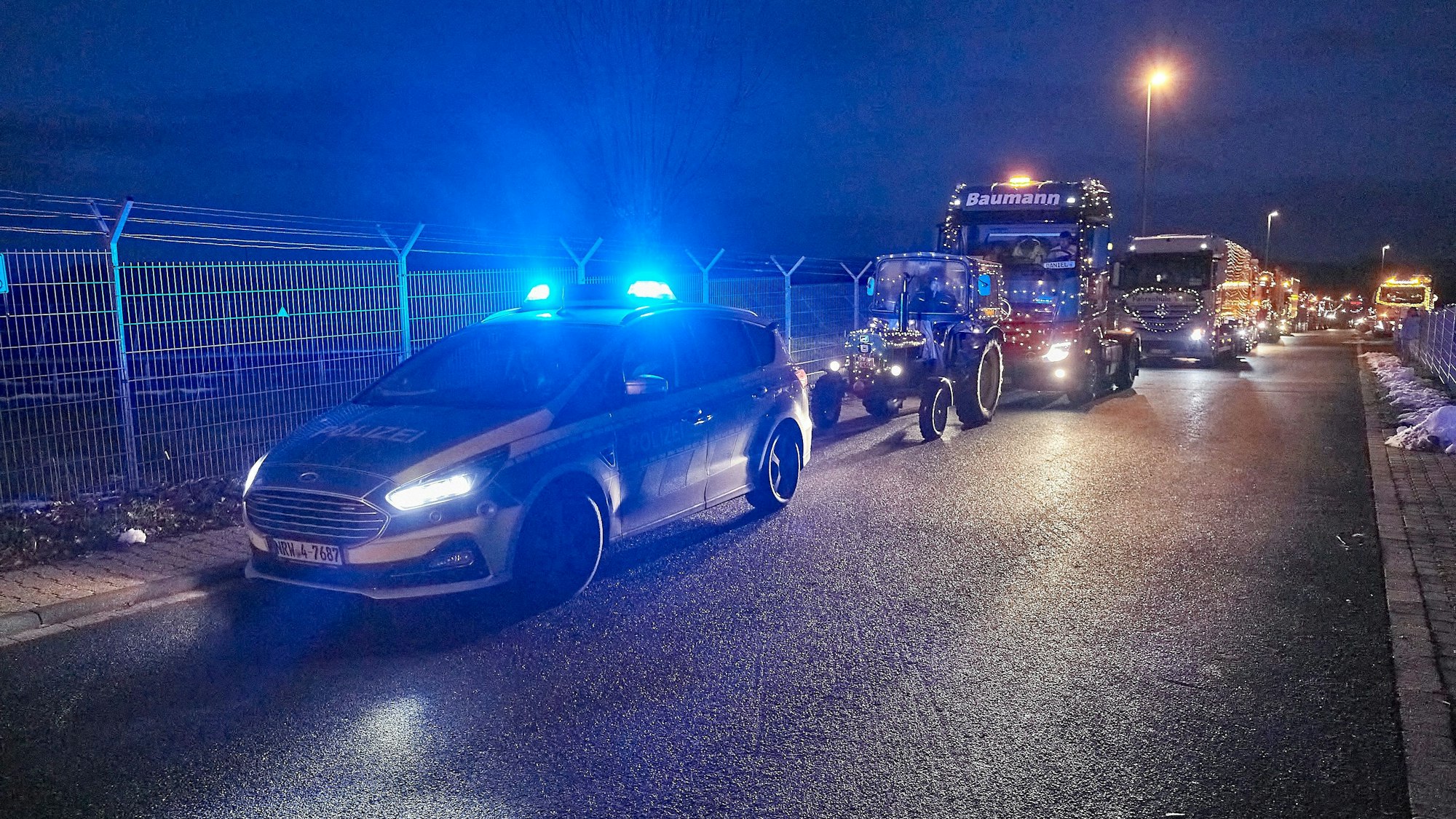 Ein Konvoi mit beleuchteten Traktoren wird von einem Polizeiwagen angeführt.