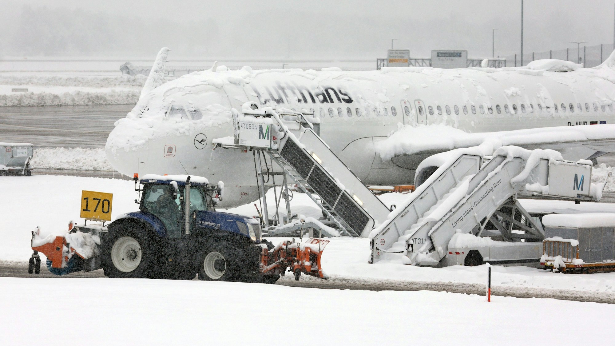 Ein Räumfahrzeug fährt vor einem eingeschneiten Airbus A320 der Lufthansa her, um die Schneemassen am Flughafen München zu beseitigen. Der Süden Deutschlands wurde von Rekord-Schneemengen getroffen.