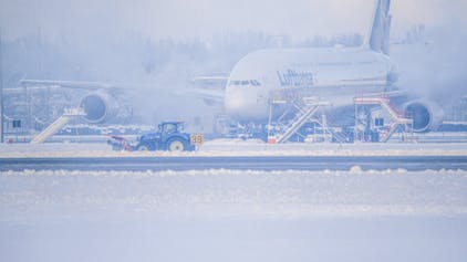 Ein Schneeräumer fährt im Schneetreiben auf dem Flughafen vor einer Maschine entlang. Wegen Eisregen konnten Flugzeuge in München stundenlang nicht starten oder landen.