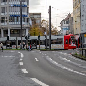 Eine Straßenbahn fährt eine leichte Kurve auf den Neumarkt zu. Fußgänger gehen über eine Straße.
