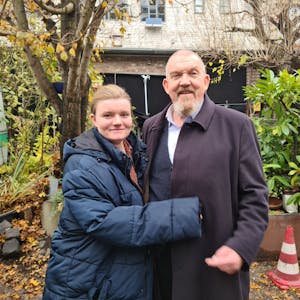 Eine junge Frau und ein älterer Mann mit Bart stehen in einem begrünten Hinterhof.