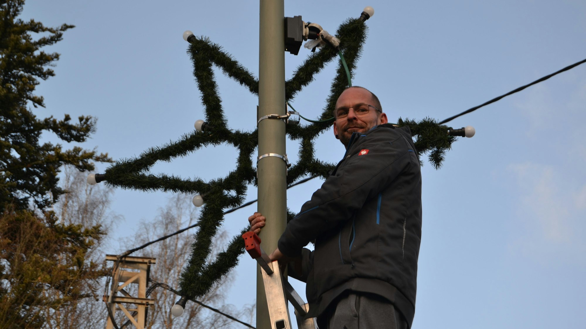 Auf einer Leiter in mehr als drei Metern Höhe steht Oliver Herrmann, der gerade einen Stern als Weihnachtsschmuck an die Straßenlaterne gehängt hat.