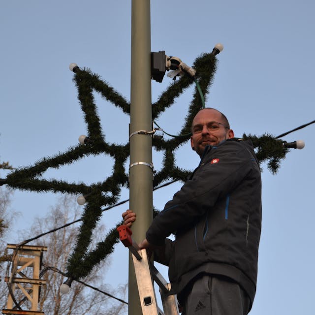 Auf einer Leiter in mehr als drei Metern Höhe steht Oliver Herrmann, der gerade einen Stern als Weihnachtsschmuck an die Straßenlaterne gehängt hat.