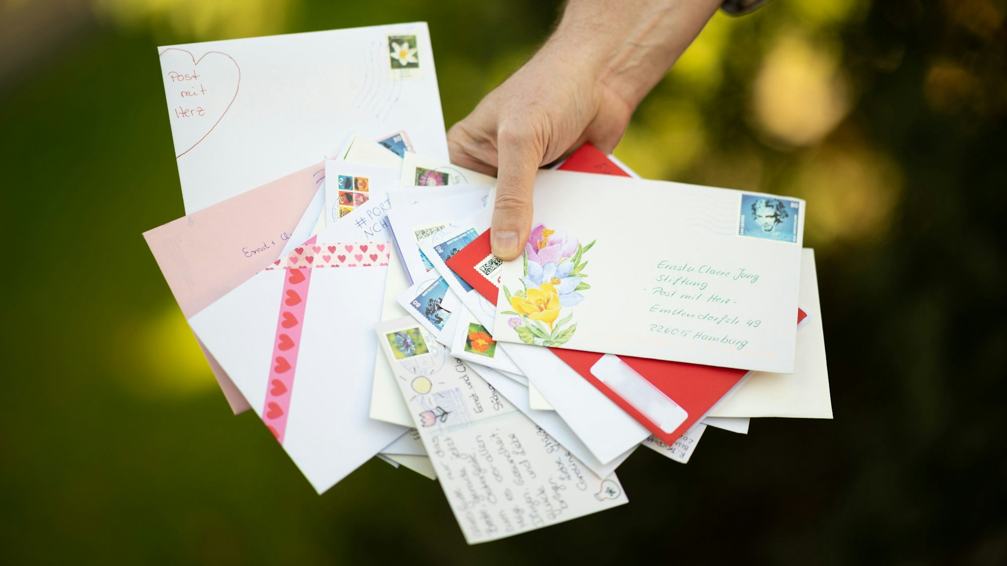 Aufgefächerte Briefumschläge mit Herzen und Blumen verziert in einer Hand.