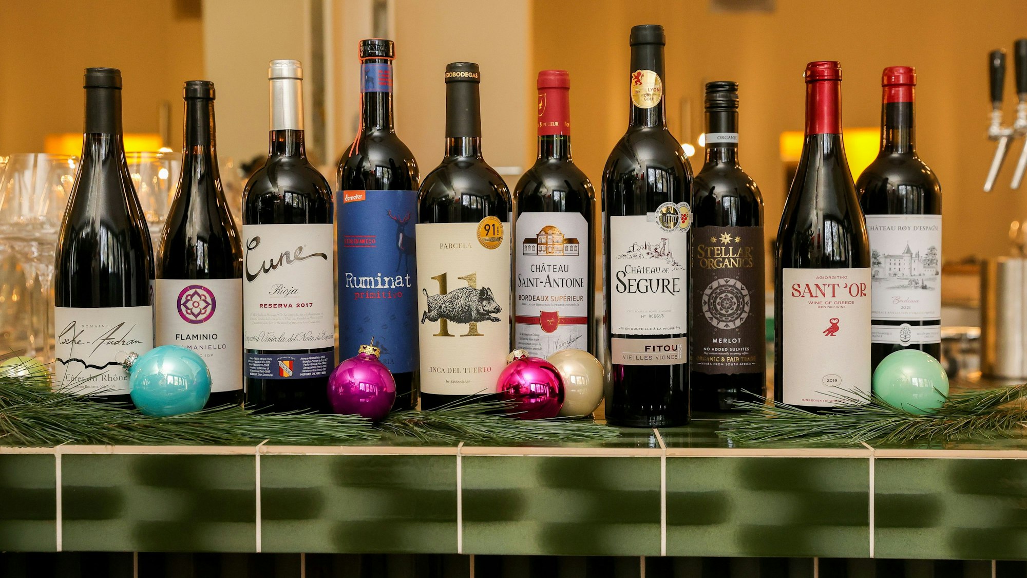 Zehn Flaschen Rotwein stehen auf einem Thekentresen, weihnachtlich geschmückt.