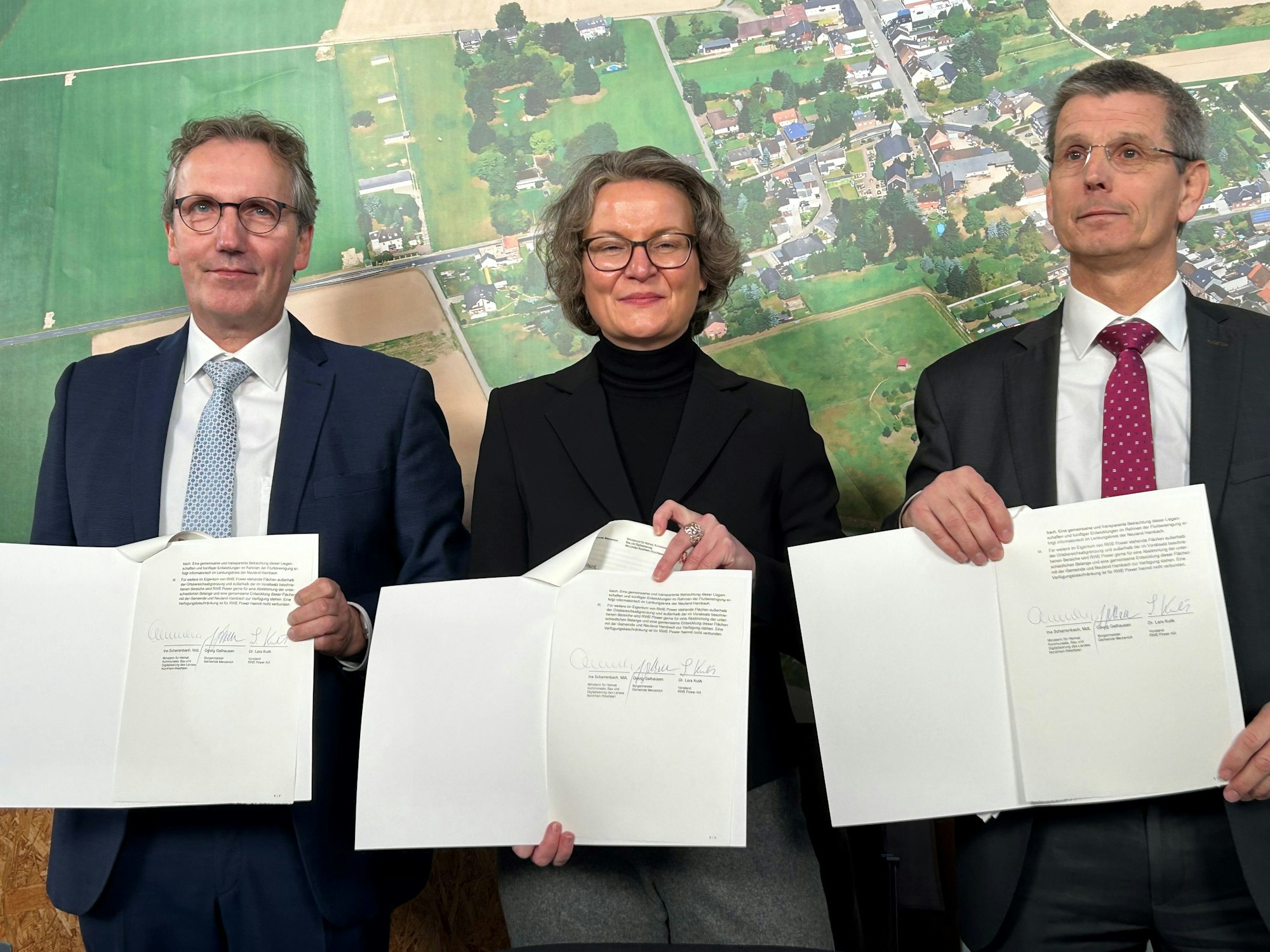 Die drei Beteiligten sind im Gruppenbild zu sehen und halten je ein Exemplar des Übergabevertrags vor sich: Merzenichs Bürgermeister Georg Gelhausen, Kommunalministerin Ina Scharrenbach und RWE-Vorstand Lars Kulik.