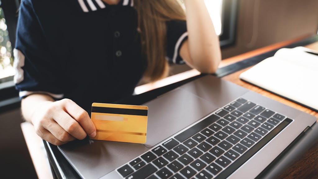 Symbolfoto: Eine Frau sitzt vor einem Laptop und hält eine Kreditkarte für das Online-Shopping bereit.&nbsp;
