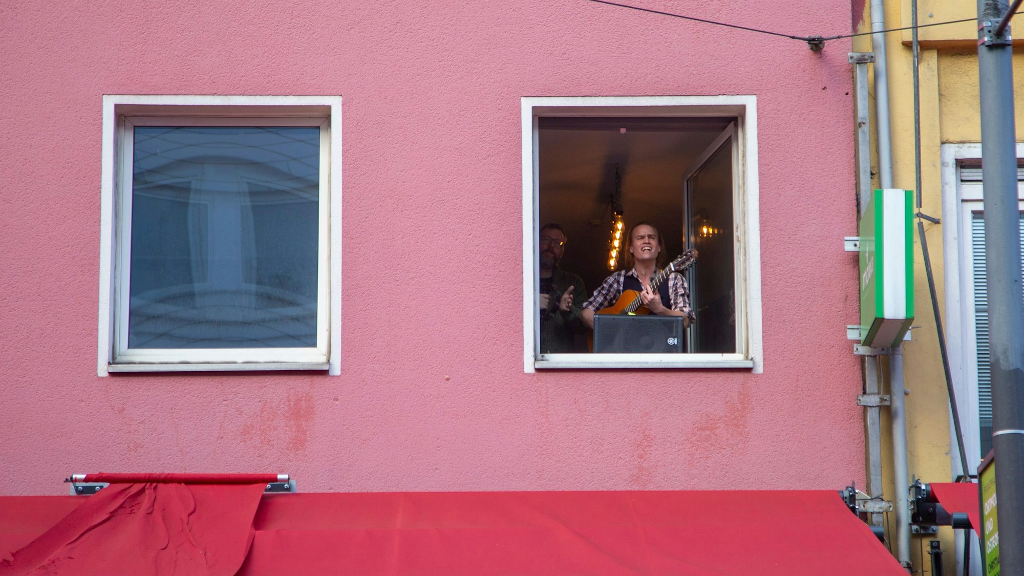 Zwei Männer singen an einem Fenster. Einer spielt Gitarre.