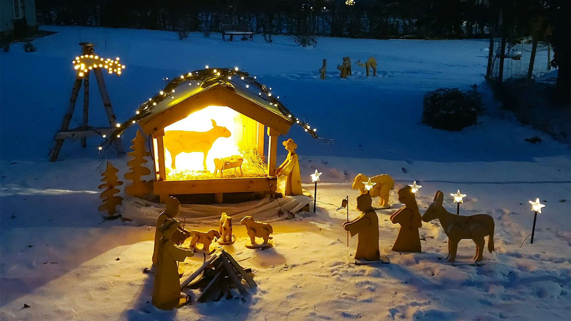 Eine beleuchtete Weihnachtskrippe mit Holzfiguren steht auf einer verschneiten Wiese in Ripsdorf.