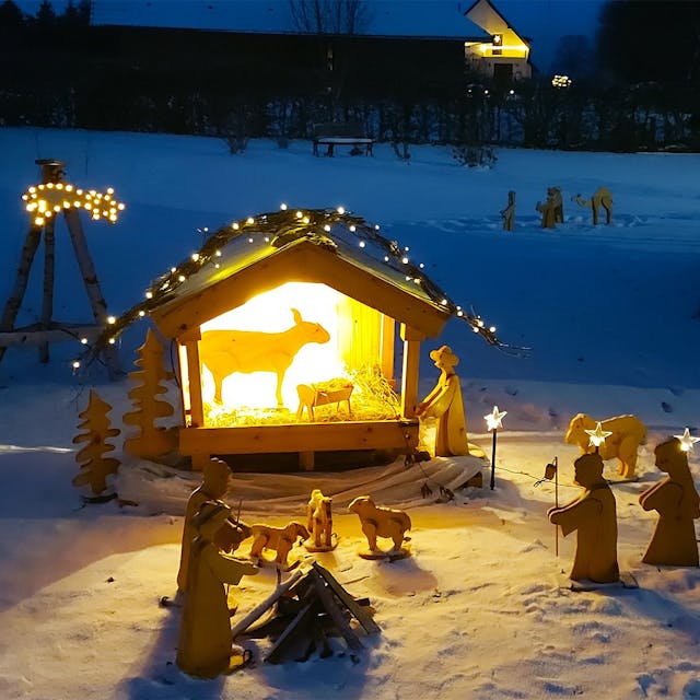 Eine beleuchtete Weihnachtskrippe mit Holzfiguren steht auf einer verschneiten Wiese in Ripsdorf.