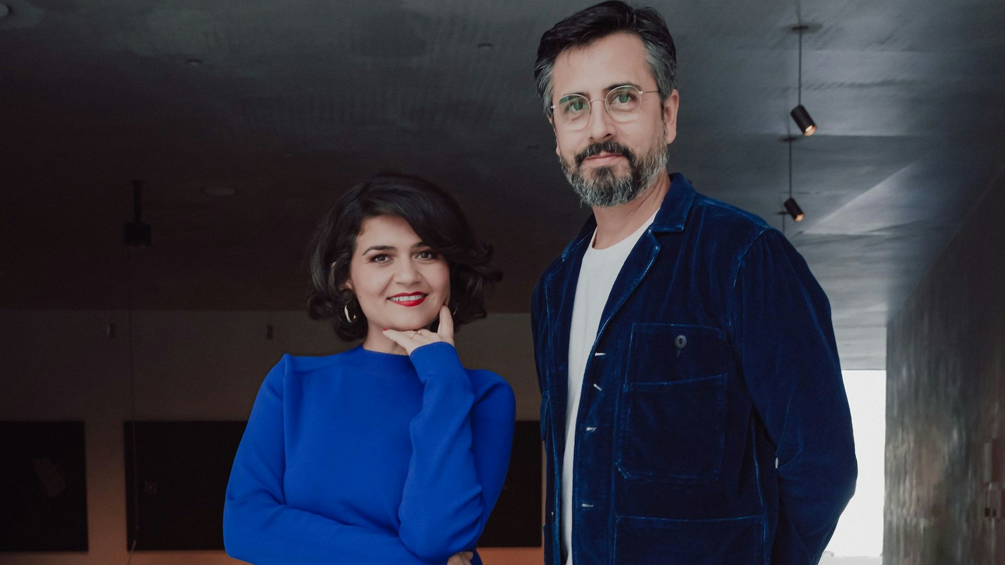 Pınar Karabulut und Rafael Sanchez blicken in die Kamera. Sie trägt einen blauen Pullover, er ein blaues Hemd.