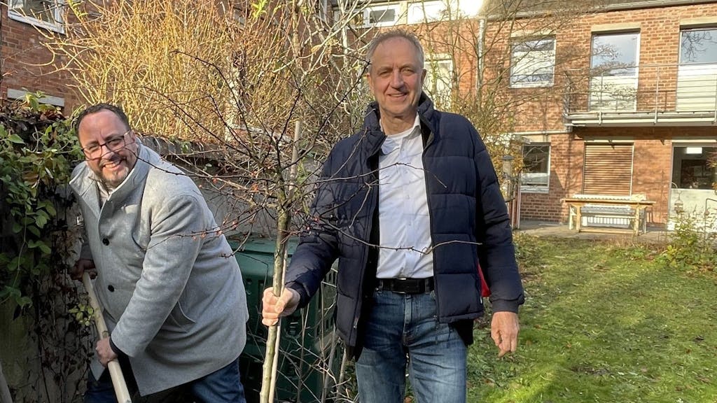 Zwei Männer stehen in einem Garten und pflanzen einen Baum.