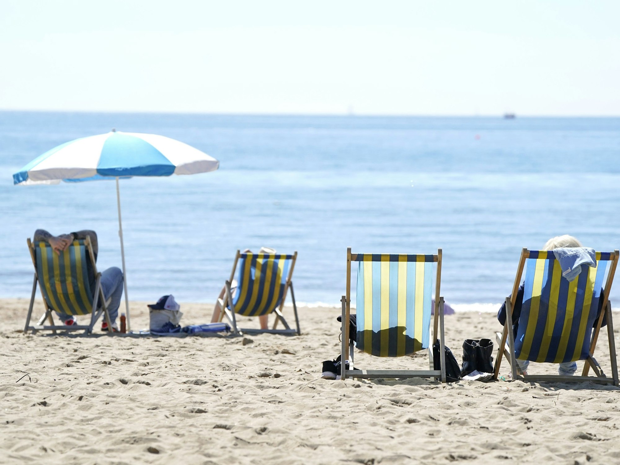 Menschen liegen am Strand von Bournemouth in Liegestühlen, hier im April 2022.
