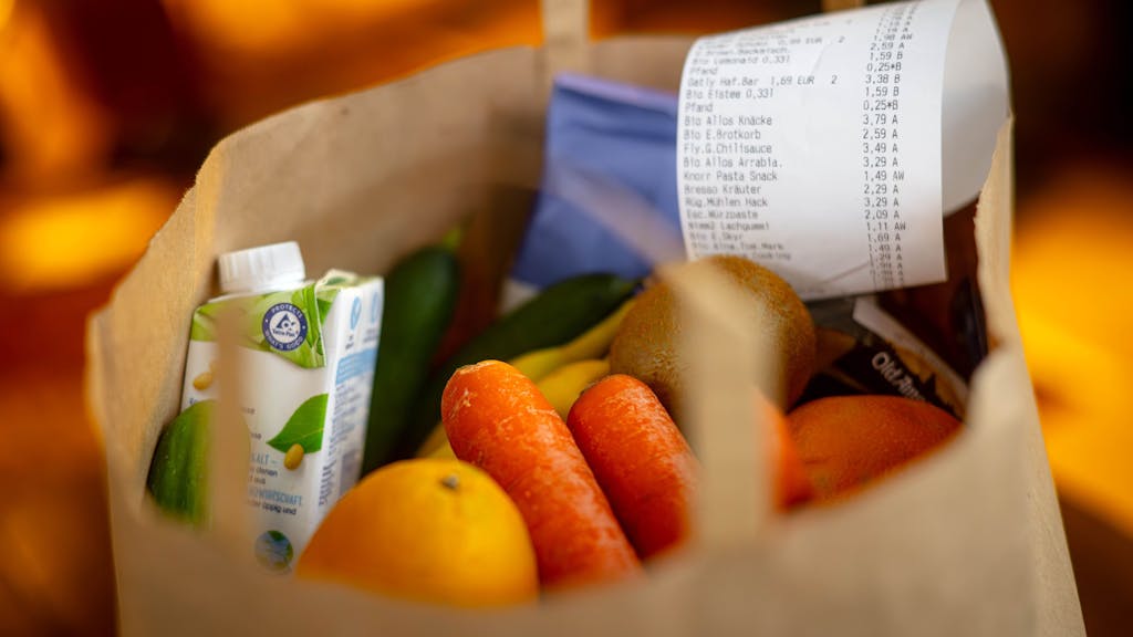 Ein Kassenbon liegt auf den Lebensmitteln in einer Einkaufstüte: Viele Supermärkte listen ihre Eigenmarken zu günstigeren Preisen als Discounter, das hat eine neue Erhebung ergeben.