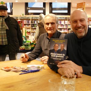 Zwei Männer an einem Tisch präsentieren ein Buch