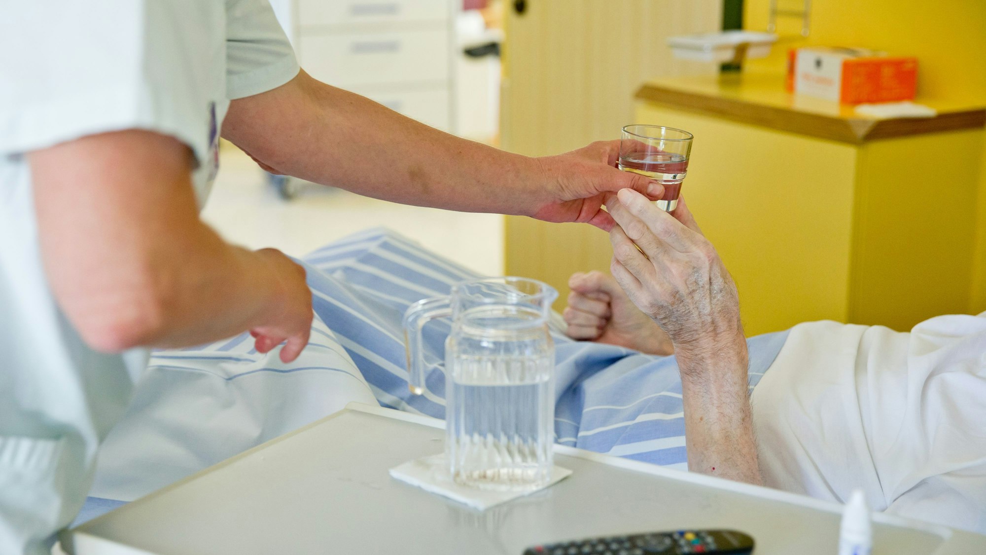 Man sieht, wie eine Pflegekraft einer Patientin ein Glas Wasser reicht.