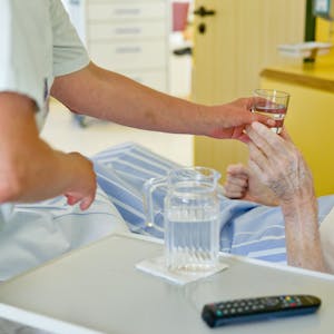 Eine Krankenpflegerin reicht einem Patienten ein Glas Wasser.&nbsp;