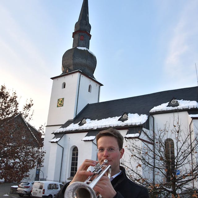 Ein Trompeter steht vor einer schneebedeckten Kirche und spielt.