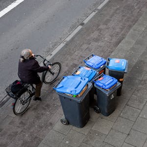Abfalltonnen mit blauem Deckel stehen zur Abholung der Kölner Abfallwirtschaftsbetriebe am Straßenrand.