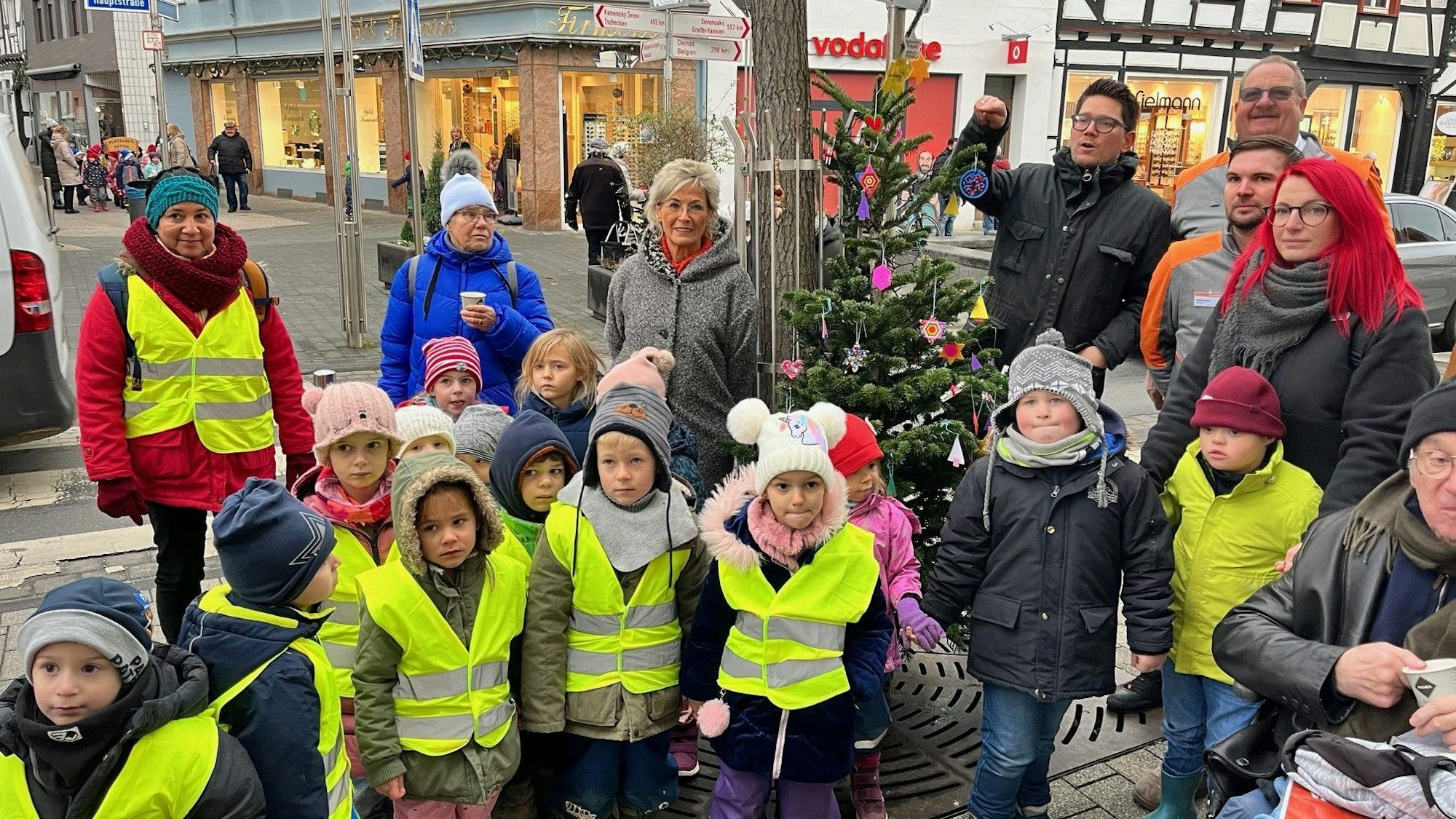 Vor einem geschmückten Weihnachtsbaum in der Rheinbacher Innenstadt stehen ein Dutzend Kinder mit Warnwesten und einige Erwachsene.