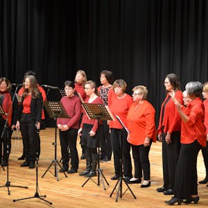 13 Frauen des Gospelchors „Go(o)d Sounds“ stehen in rot und schwarz auf einer Bühne und singen.