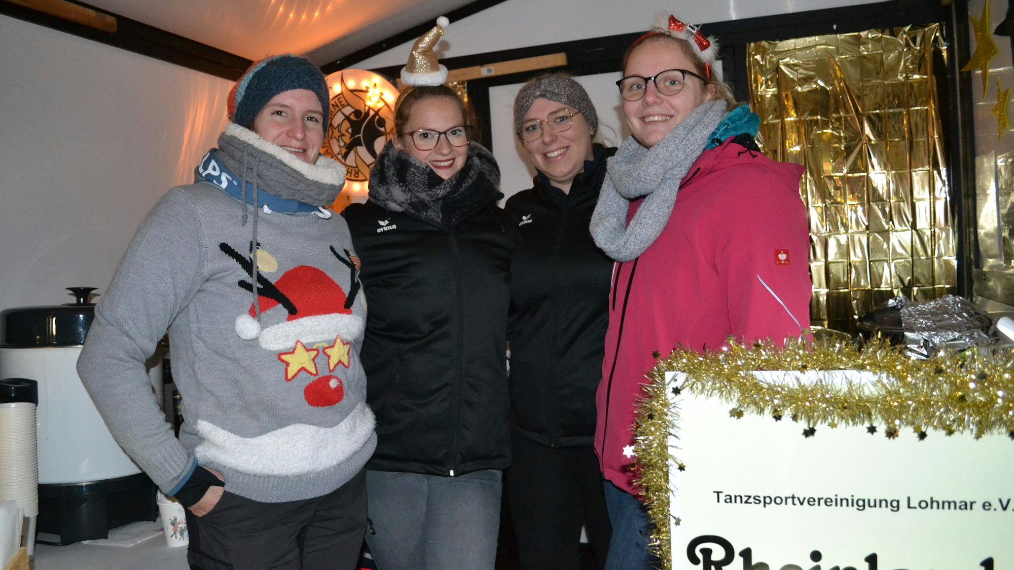 Vier junge Frauen an einem weihnachtlich dekoriertem Glühweinstand.