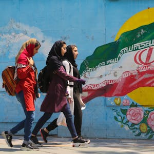Junge Mädchen laufen vor einem Wandgemälde mit der iranischen Nationalflagge im Zentrum der Hauptstadt Teheran.