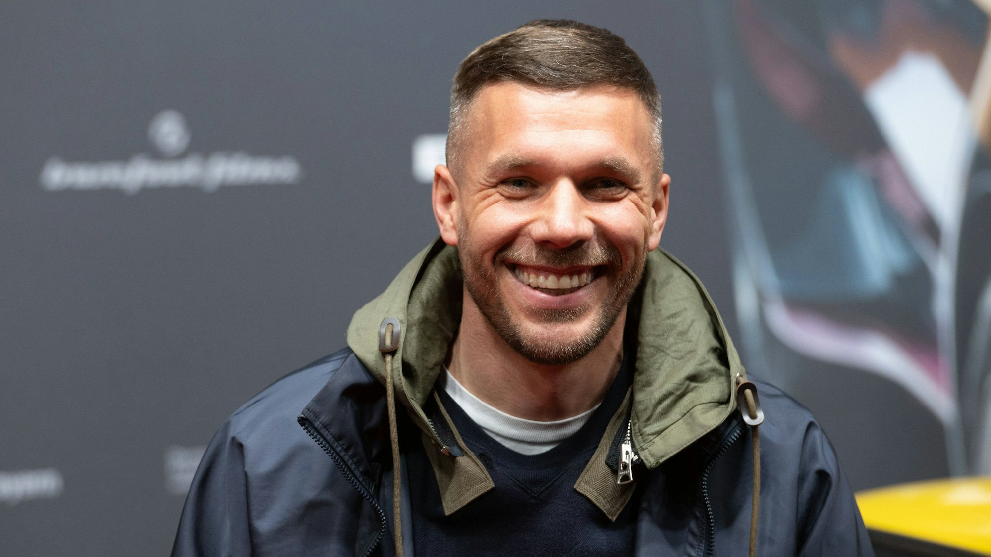 Lukas Podolski lacht bei einer Filmpremiere auf dem Roten Teppich.